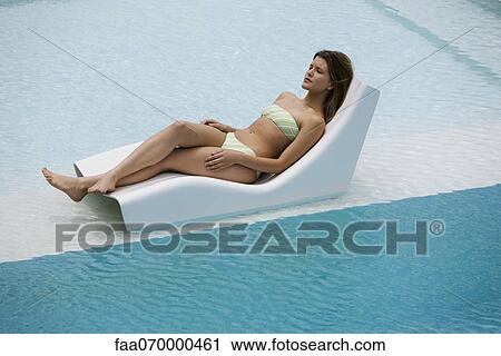 Stock Image - Young woman sunbathing by pool. Fotosearch