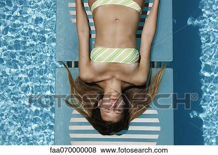 Stock Photo - Young woman sunbathing by pool. Fotosearch