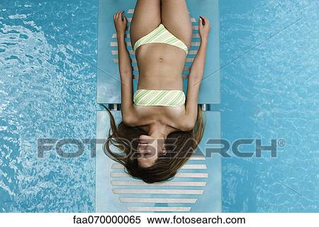 Stock Photography - Young woman sunbathing by pool. Fotosearch