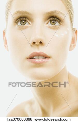 Stock Photograph - Young woman with dollops of undereye cream on face, portrait, close-up. Fotosearch