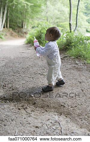 Baby girl holding baby bottle in woods View Large Photo Image Picture - Baby girl holding baby bottle in woods. Fotosearch