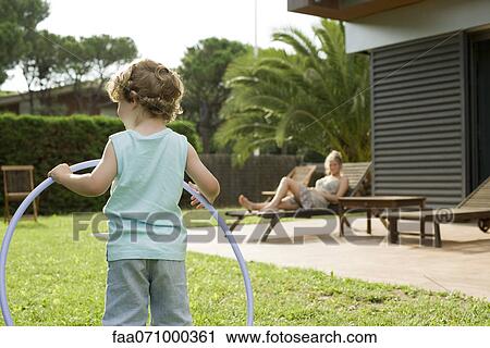 Boy holding plastic hoop, mother relaxing in background View Large Photo Image Stock Image - Boy holding plastic hoop, mother relaxing in background. Fotosearch