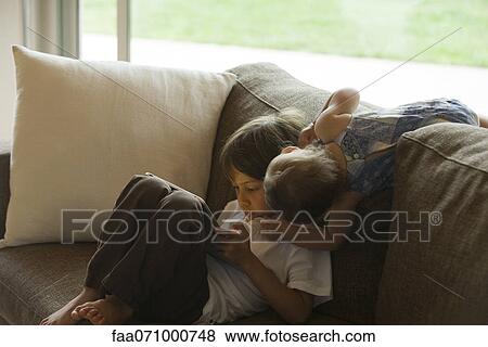 Boy relaxing on sofa, looking at digital tablet View Large Photo Image Stock Photo - Boy relaxing on sofa, looking at digital tablet. Fotosearch