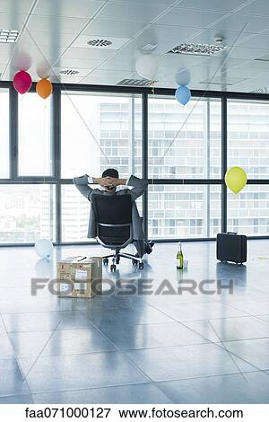 Stock Photo - Businessman sitting in new office with balloons and box. Fotosearch