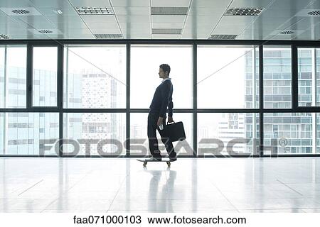 Stock Image - Businessman standing on skateboard with briefcase. Fotosearch