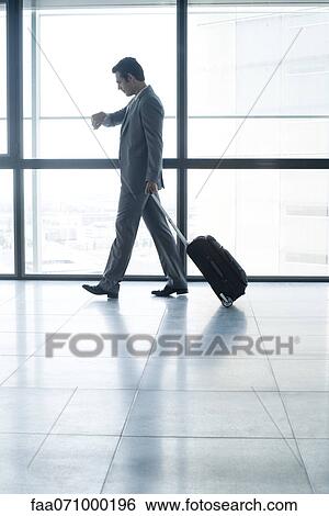 Stock Photograph - Businessman with wheeled suitcase looking at watch. Fotosearch