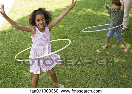 Stock Image - Children playing with plastic hoop outdoors. Fotosearch
