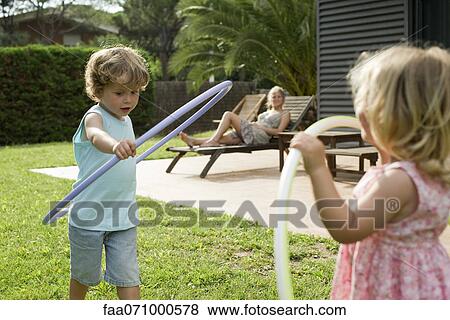 Children playing with plastic hoops while mother watches in background View Large Photo Image Stock Photo - Children playing with plastic hoops while mother watches in background. Fotosearch