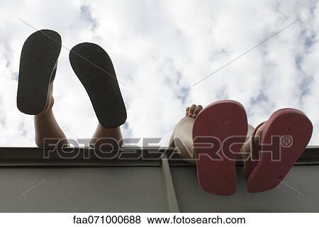 Stock Photo - Children's feet dangling over ledge, low angle view. Fotosearch