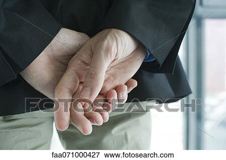 Stock Photo - Clasped hands behind back, rear view, cropped. Fotosearch