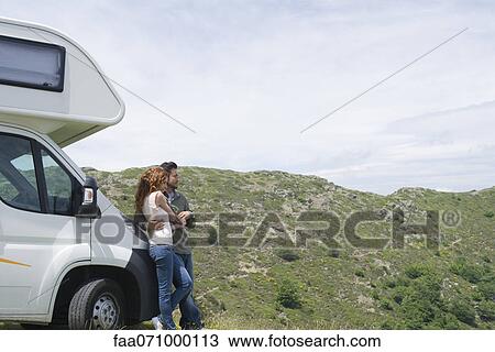 Stock Image - Couple embracing by motor home, enjoying scenic view. Fotosearch