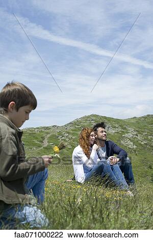 Couple sitting on meadow, boy picking flowers in foreground View Large Photo Image Stock Image - Couple sitting on meadow, boy picking flowers in foreground. Fotosearch