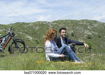 Couple sitting on meadow by mountain bikes View Large Photo Image Stock Image - Couple sitting on meadow by mountain bikes. Fotosearch