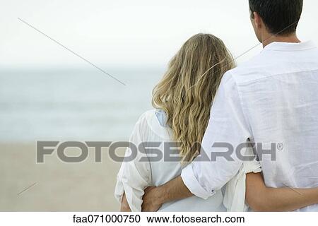 Couple standing together at beach, rear view View Large Photo Image Stock Image - Couple standing together at beach, rear view. Fotosearch