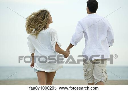 Couple walking hand in hand at the beach, rear view View Large Photo Image Stock Photography - Couple walking hand in hand at the beach, rear view. Fotosearch