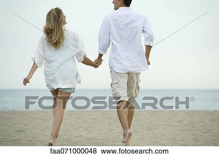 Couple walking hand in hand on beach, rear view View Large Photo Image Stock Photo - Couple walking hand in hand on beach, rear view. Fotosearch