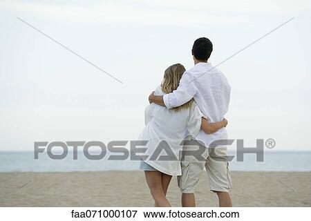 Stock Photo - Couple walking together at the beach, rear view. Fotosearch