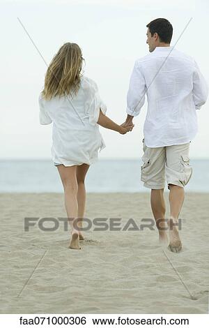 Couple walking together on beach, rear view View Large Photo Image Stock Photograph - Couple walking together on beach, rear view. Fotosearch