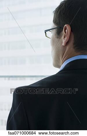 Executive looking out window, rear view View Large Photo Image Picture - Executive looking out window, rear view. Fotosearch