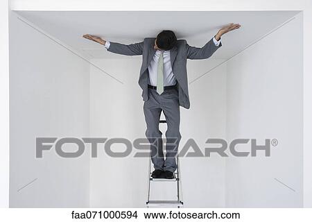 Executive standing on stepladder, arms outstretched on ceiling View Large Photo Image Picture - Executive standing on stepladder, arms outstretched on ceiling. Fotosearch