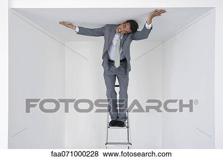 Executive standing on stepladder, pushing ceiling View Large Photo Image Stock Photo - Executive standing on stepladder, pushing ceiling. Fotosearch