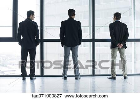 Executives standing side by side, looking out window View Large Photo Image Stock Photo - Executives standing side by side, looking out window. Fotosearch