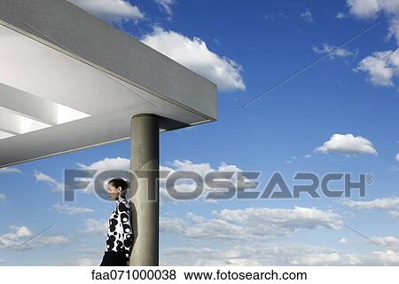 Stock Photo - Fashionably dressed young woman leaning against portico column. Fotosearch