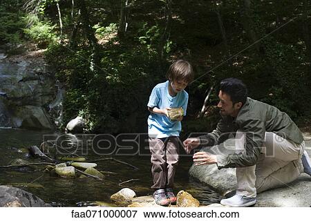 Stock Photo - Father and son exploring nature, boy holding rock. Fotosearch