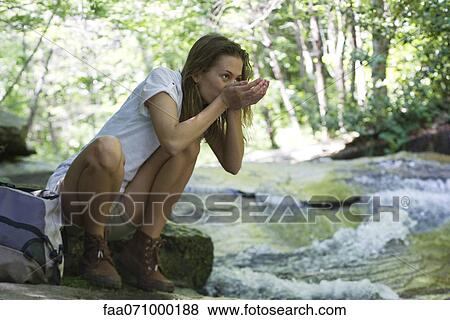 Stock Photo - Female hiker drinking water from stream. Fotosearch