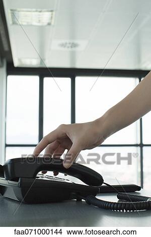 Picture - Hand picking up telephone receiver, backlit, cropped. Fotosearch