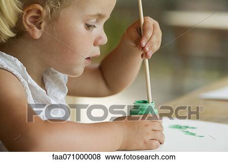 Stock Photo - Little girl dipping paintbrush into paint. Fotosearch