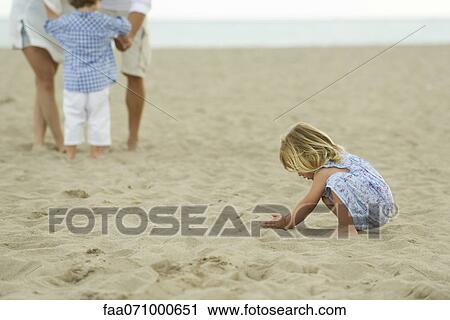 Little girl playing in sand at the beach, family in background View Large Photo Image Stock Image - Little girl playing in sand at the beach, family in background. Fotosearch