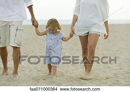 Little girl walking on beach with her parents, cropped View Large Photo Image Picture - Little girl walking on beach with her parents, cropped. Fotosearch