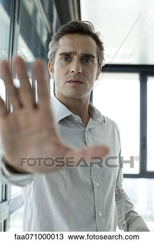 Stock Image - Man holding hand up in front of camera, backlit. Fotosearch