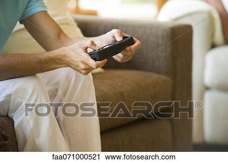 Stock Image - Man playing video game using wireless controller, cropped. Fotosearch