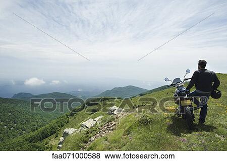 Man standing by motorcycle on top of mountain, rear view View Large Photo Image Stock Photo - Man standing by motorcycle on top of mountain, rear view. Fotosearch