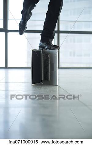 Stock Photography - Man standing on top of laptop computer, low section. Fotosearch