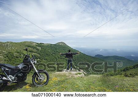 Stock Image - Man standing on top of rock with arms outstretched, rear view. Fotosearch
