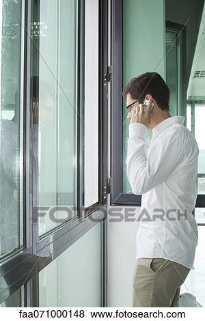 Stock Photo - Man talking on cell phone by window. Fotosearch