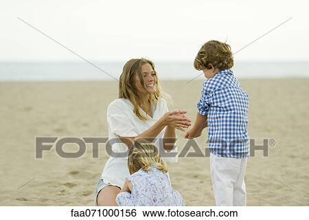 Stock Photograph - Mother and children playing in sound at the beach. Fotosearch
