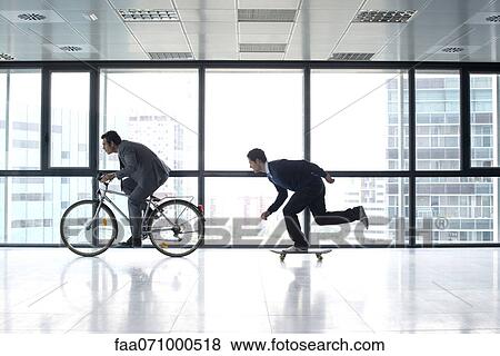 One businessman riding bicycle, the other skateboarding View Large Photo Image Stock Photo - One businessman riding bicycle, the other skateboarding. Fotosearch