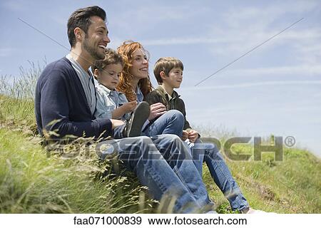 Stock Photo - Parents with young boys sitting on meadow. Fotosearch