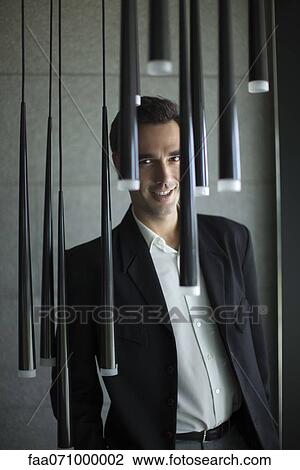 Smiling businessman standing behind pendant lights View Large Photo Image Stock Image - Smiling businessman standing behind pendant lights. Fotosearch
