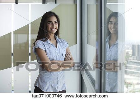 Stock Photograph - Smiling woman standing by window with arms folded. Fotosearch
