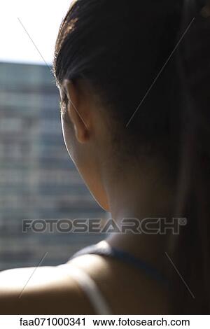Stock Image - Woman by window, rear view, backlit. Fotosearch
