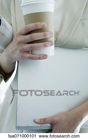 Stock Image - Woman holding disposable coffee cup, mid section. Fotosearch