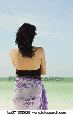 Stock Photography - Woman on beach looking at view, rear view. Fotosearch