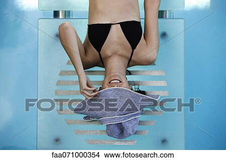 Picture - Woman reclining poolside, concealing face with brim of sun hat. Fotosearch