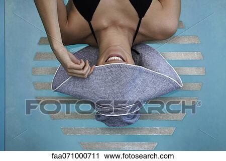 Stock Image - Woman reclining poolside, concealing face with brim of sun hat. Fotosearch