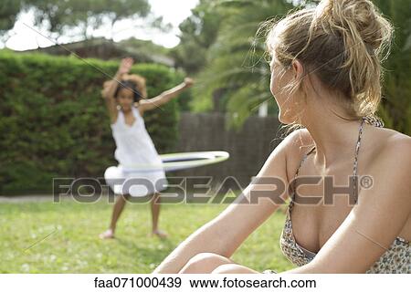 Woman sitting outdoors, watching child playing with plastic hoop View Large Photo Image Stock Photo - Woman sitting outdoors, watching child playing with plastic hoop. Fotosearch